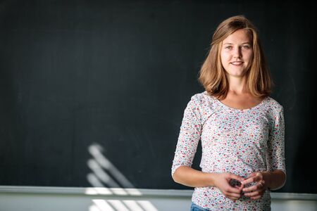 Pretty, young female student/young teacxher in front of a blackboard during classの写真素材