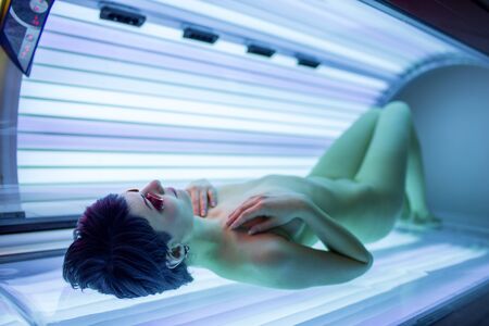 Pretty, young woman tanning her skin in a modern solarium (shallow DOF; color toned image)