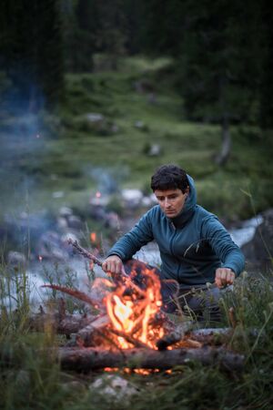 Young man making fire while camping outdoors, in an alpine wildernessの写真素材