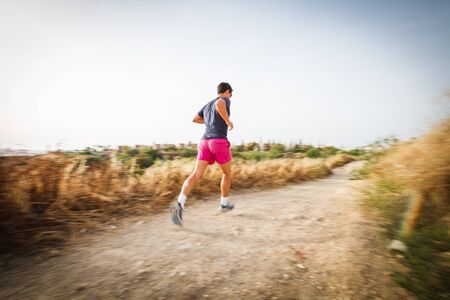 Caucasian young man running on a seacost path on a lovely summer evening, training for marathon...