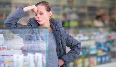 Young woman looking for the right pills in a modern pharmacy - surprised by the prices of these pharamceuticals (shallow DOF; color toned image)の写真素材