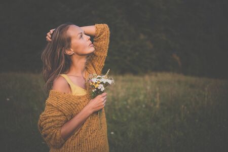 Beautiful young woman outdoors with a bouquet of wild flowers in a field, enjoying nature. Happy Woman on spring meadowの写真素材