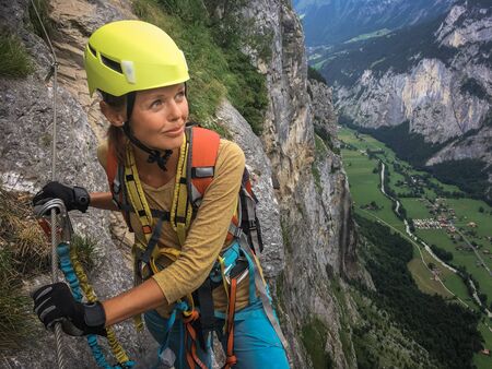 Pretty, female climber on a via ferrata - climbing on a rock in Swiss Alpsの写真素材