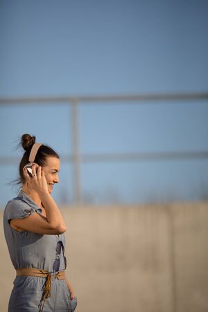 Pretty, young woman with headphones standing against concrete wall, enjoyig the hi-fi quality sound, listening to her favorite songs (color toned image)の写真素材