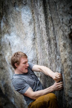 A rock climber climbing on a boulder rock outdoors. Group of friends involved in sports outside.の写真素材