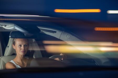 Young female driver driving her car at night (color toned image; shallow DOF)の写真素材