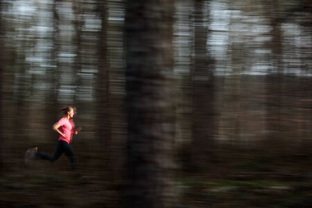 Young woman running outdoors in a forest, going fast (motion blurred image)の写真素材