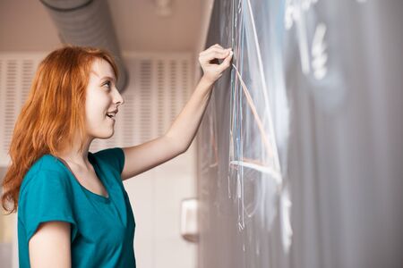 Portrait of a pretty young college student writing on the blackboard during a maths class (color...