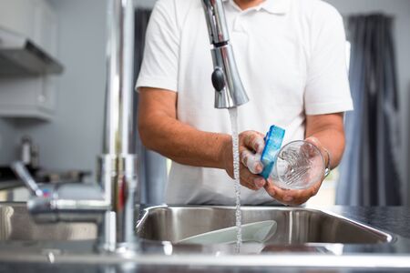 Senior man washing dishes in his modern, bright kitchen (shallow DOF; color toned image)の写真素材