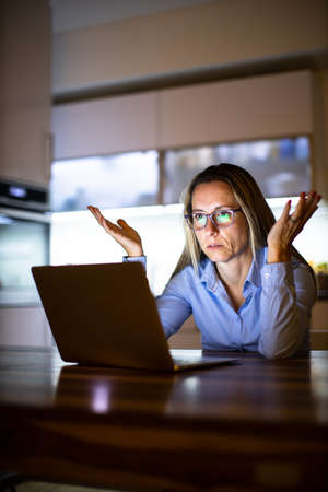 Pretty, middle-aged woman working late in the day on a laptop computer at home, running a business...