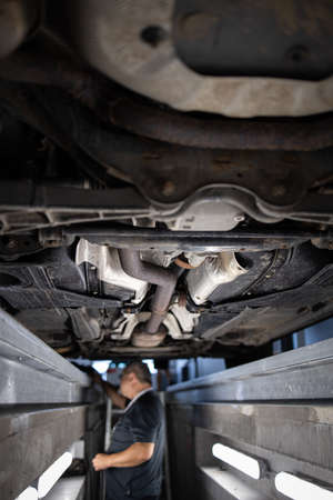 Car mechanic under a car in a repair shop/car garage (shallow DOF/color toned image)の写真素材