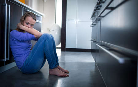 Depressed young woman, sitting on the kitchen floor, feeling down