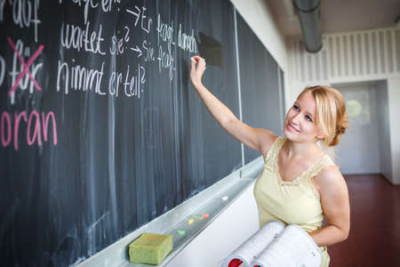 Pretty young teacher writing on the chalkboard/blackboard during class (shallow DOF; color toned...