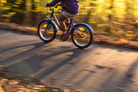 Little boy going fast on his little bike on a forest path in warm evening lightの写真素材