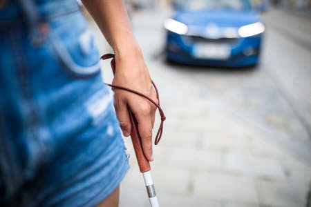 Blind woman walking on city streets, using her white cane to navigate the urban space better and to get to her destination safelyの写真素材