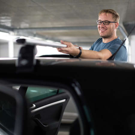 Handsome young driver getting ready to go biking - putting a bike rack on the roof of his carの写真素材