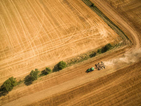 Aerial view of a tractor working a field after harvestの写真素材