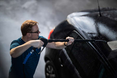 Young man washing his beloved car carefully in a manual car wash to prevent any damage and detail it properlyの写真素材