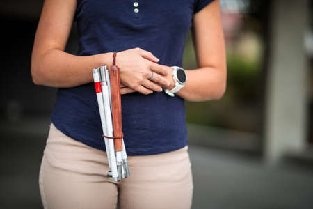 Blind woman walking on city streets, using her white cane to navigate the urban space better and to get to her destination safelyの写真素材