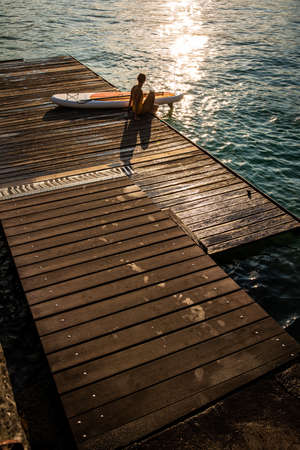 SUP Stand up paddle board concept - Pretty, young woman paddle boarding on a lovely lake in warm late afternoon lightの写真素材