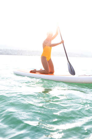 SUP Stand up paddle board concept - Pretty, young woman paddle boarding on a lovely lake in warm late afternoon lightの写真素材