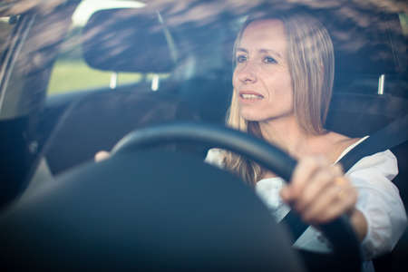 Pretty middle aged woman at the steering wheel of her carの写真素材