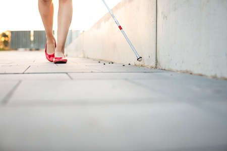 Blind woman walking on city streets, using her white cane to navigate the urban space better and to get to her destination safelyの写真素材