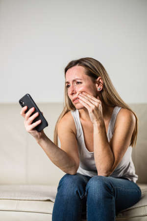 Mid-aged woman touching her cheek/mouth with painful expression because of toothache/dental issueの写真素材
