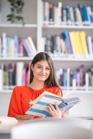 Pretty, young college student looking for a book in the library, studying for her examの写真素材