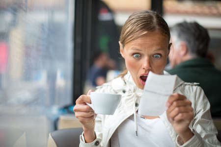Pretty, young woman baffled with the bill in a coffee shop/restaurantの写真素材