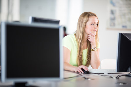 Pretty, female student looking at a desktop computer screen, learning unpleasant news about her exam results. University/office/school conceptの写真素材