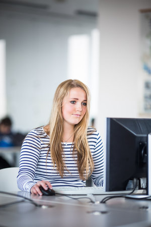 Pretty, female student looking at a desktop computer screen, learning unpleasant news about her exam results. University/office/school conceptの写真素材