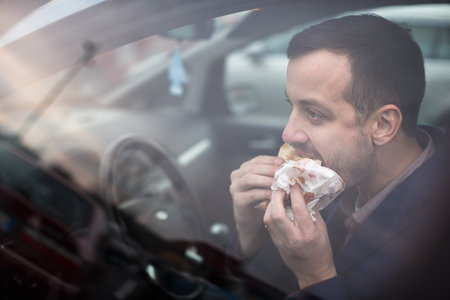 Handsome young man eating a hurried lunch in his car (color toned image; shallow DOF)の写真素材