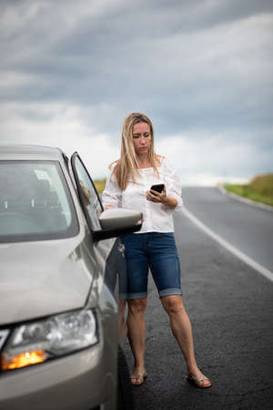 Pretty midle aged woman having car troubles - broken down car on the side of the road, calling the insurance company for assistanceの写真素材