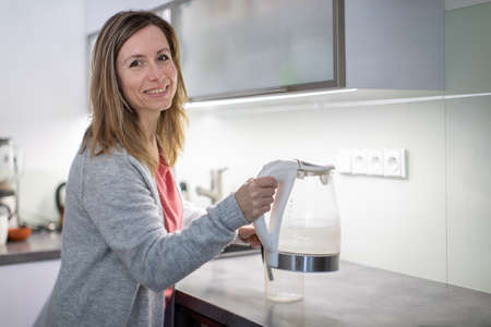 Pretty, young woman in her modern bright kitchen - making tea, healthy eating concept, household lifestyle conceptの写真素材