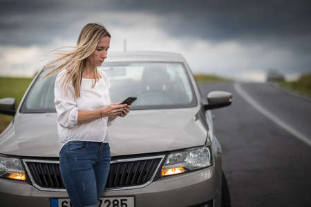Pretty midle aged woman having car troubles - broken down car on the side of the road, calling the insurance company for assistanceの写真素材