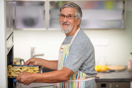 Senior man prepares healthy version of potatoes in the ovenの写真素材