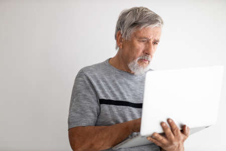 Senior man using a laptop computer at home, struggling with techology a bit, shopping online during COVID confinement/lockdown/quarantineの写真素材