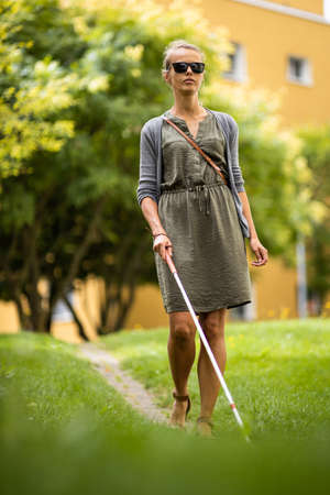 Blind woman walking on city streets, using her white cane to navigate the urban space better and to get to her destination safelyの写真素材