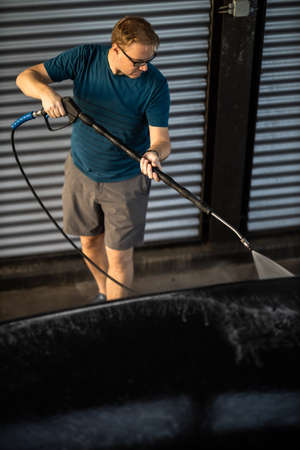 Young man washing his beloved car carefully in a manual car wash to prevent any damage and detail it properlyの写真素材