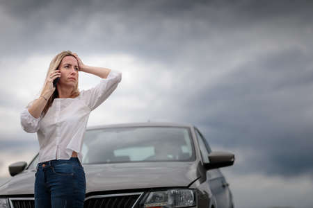 Pretty midle aged woman having car troubles - broken down car on the side of the road, calling the insurance company for assistanceの写真素材