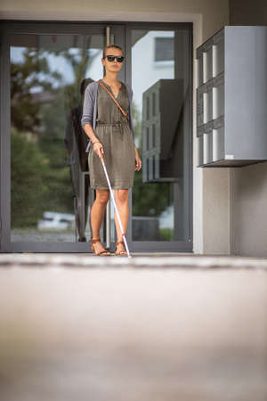 Blind woman walking on city streets, using her white cane to navigate the urban space better and to get to her destination safelyの写真素材
