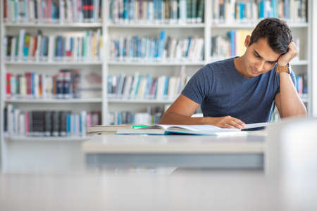 Students in a library - handsome student reading a book for his class in a bright modern libraryの写真素材