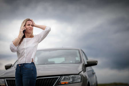 Pretty middle aged woman having car troubles - broken down car on the side of the road, calling the insurance company for assistanceの写真素材