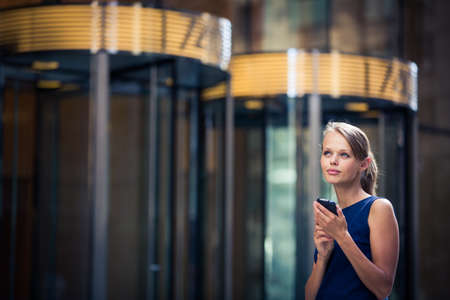 Gorgeous young businesswoman calling on her phone in front of her company's building (shallow DOF; color toned image)の写真素材