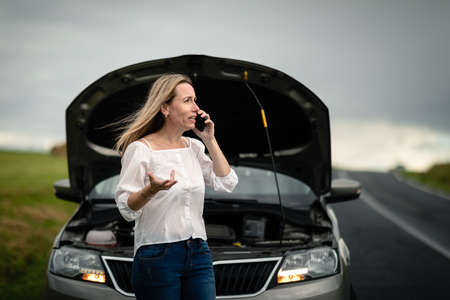 Pretty middle aged woman having car troubles - broken down car on the side of the road, calling the insurance company for assistanceの写真素材