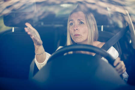 Middle aged woman at the steering wheel of her car, getting angryの写真素材