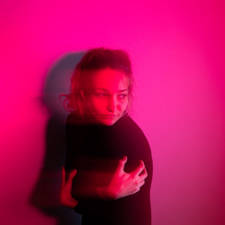 Depressed young woman in front of a wall lit by red light, lonely, anxious (color toned image)の写真素材