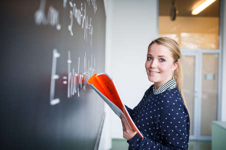 pretty young college student writing on the chalkboard/blackboard during a math classの写真素材