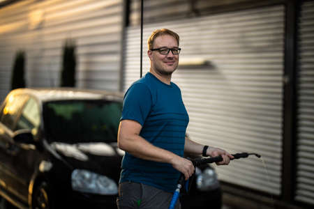 Young man washing his beloved car carefully in a manual car wash to prevent any damage and detail it properlyの写真素材